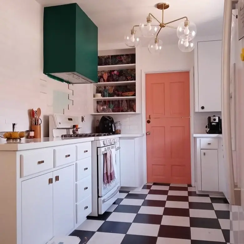 Bright kitchen with white cabinetry, a deep green range hood, coral door, and black-and-white checkerboard floor.