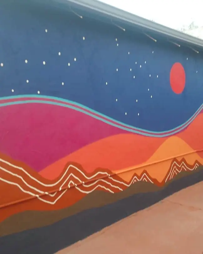 Night-sky mural with a red circle, small stars, sweeping pink and orange hills, and fine white mountain lines.