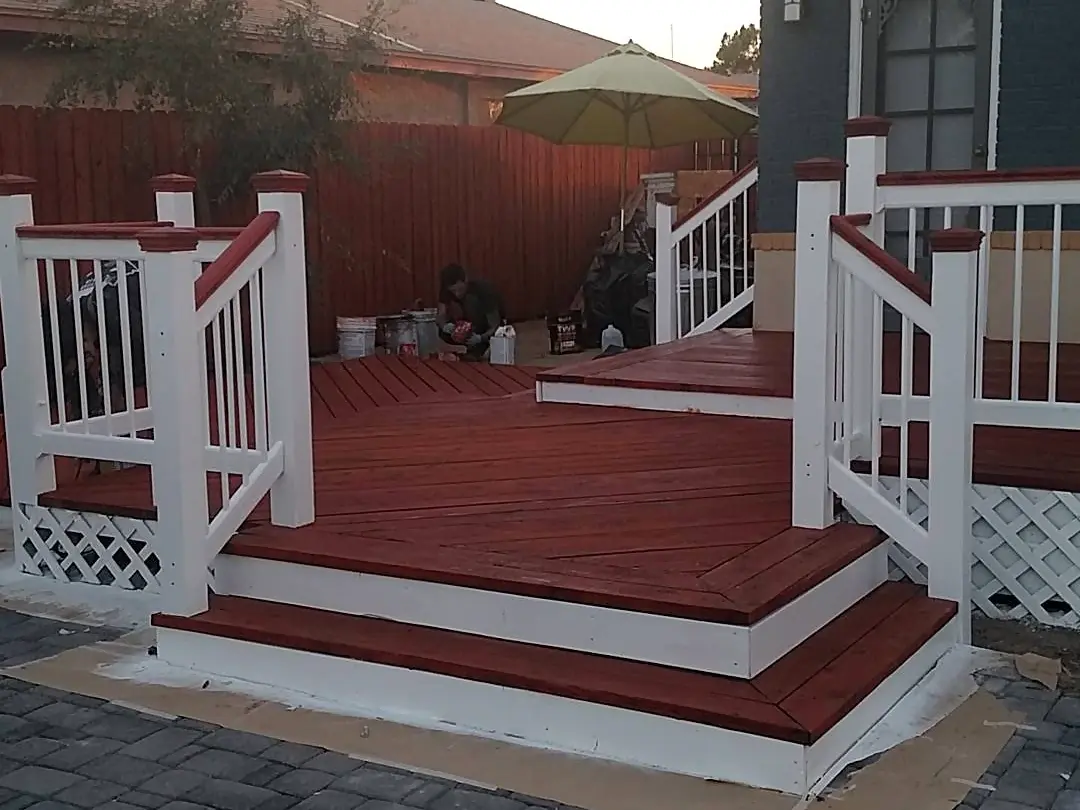 Finished red deck with crisp white railings and steps wrapping a dark gray home.