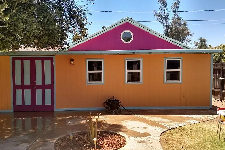 Backyard studio after painting, with an orange facade, magenta gable and doors, and pale blue-gray trim.