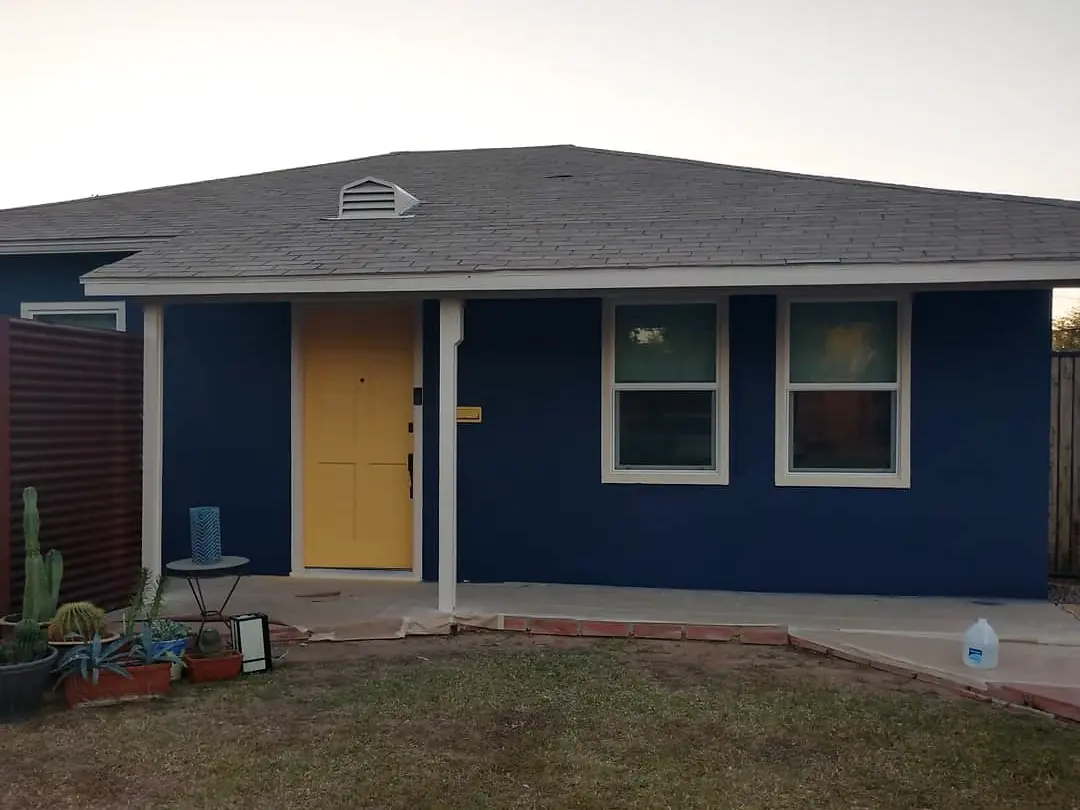 Single-story home after painting, with a navy facade, white trim, and a yellow front door.
