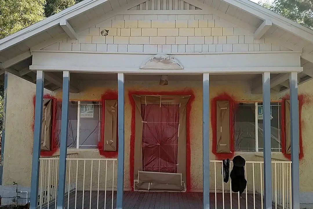 Craftsman porch during preparation, with the door and windows masked and red trim paint visible around the openings.