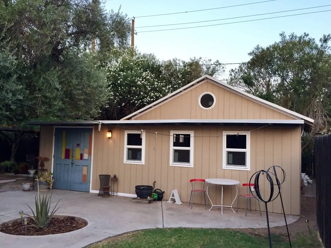 Tan backyard studio with gray doors and trim before its colorful exterior transformation.