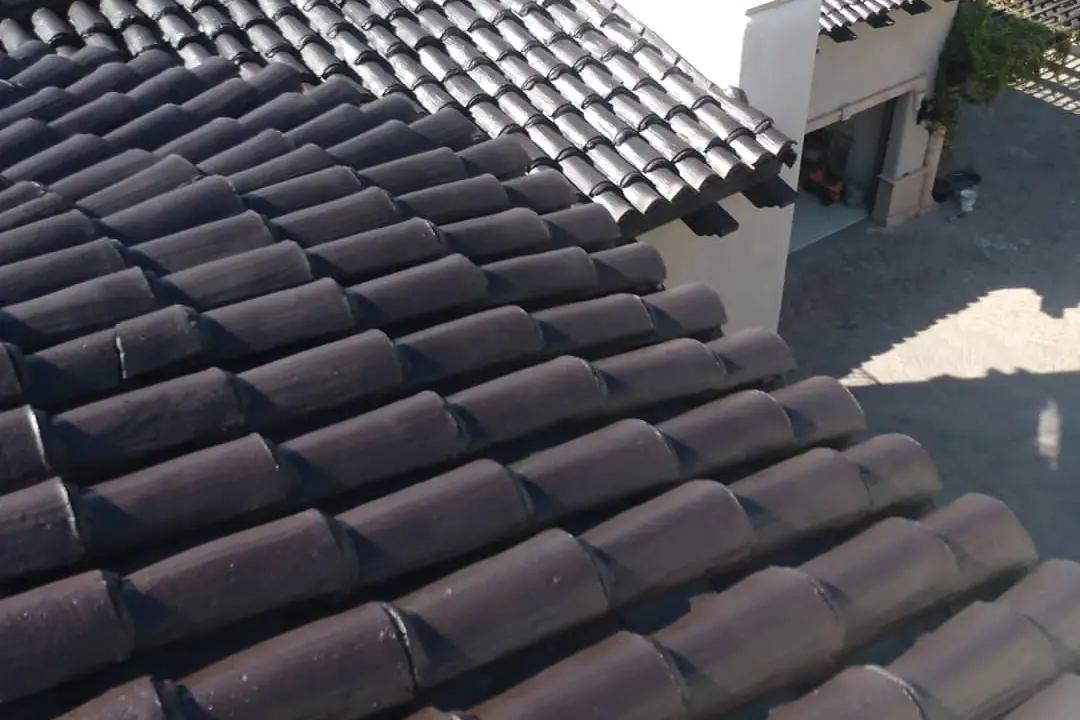 Close view across rows of freshly coated dark barrel roof tiles in bright sunlight.