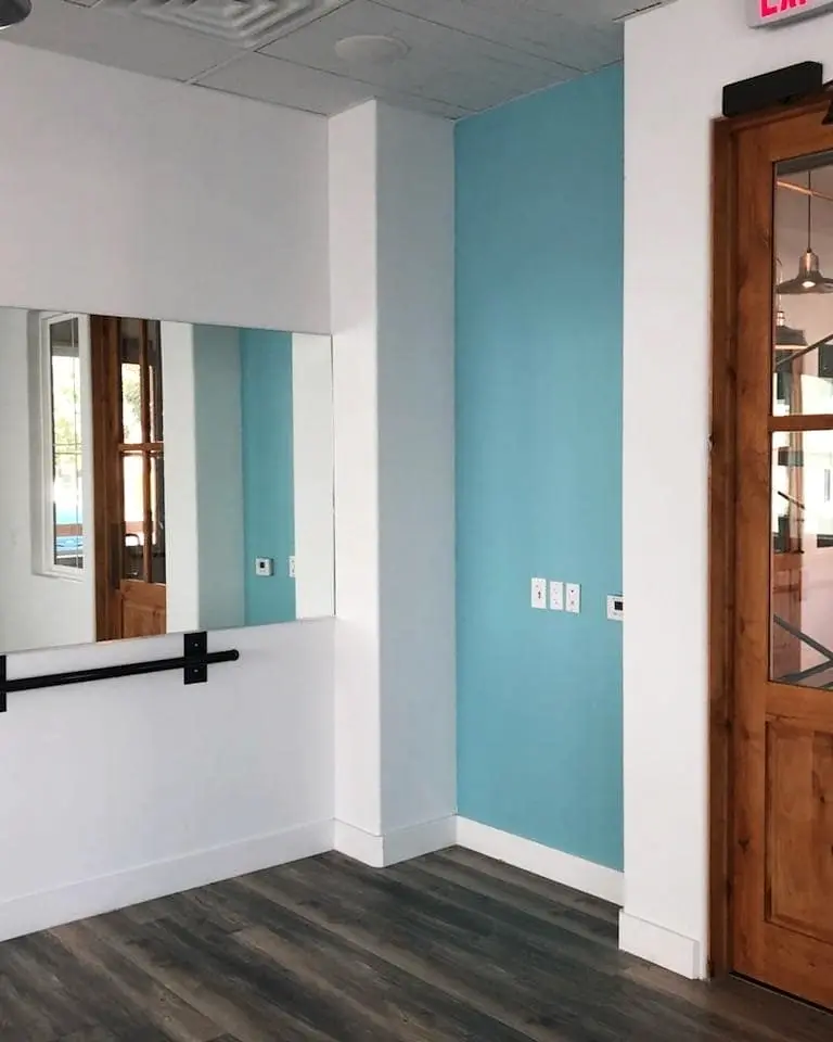 Finished yoga studio with white and aqua walls, dark wood flooring, a full-length mirror, and a wood door.