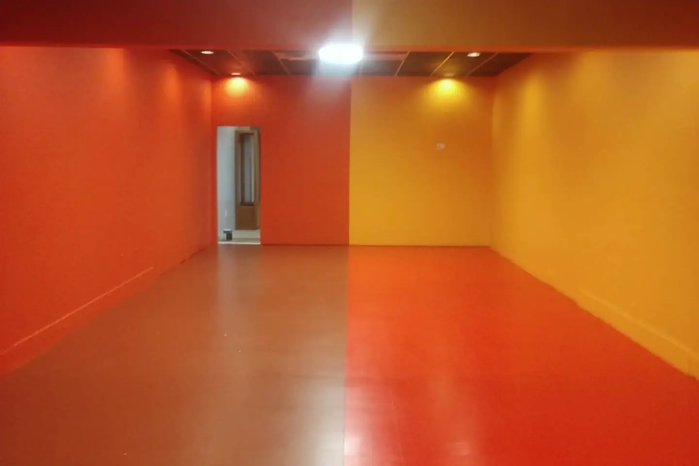 Empty commercial room finished in saturated orange, red, and yellow beneath exposed ceiling beams.