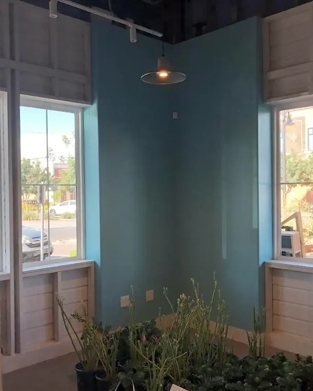 Teal-painted yoga studio corner between two tall windows, with exposed ceiling structure and a hanging light.