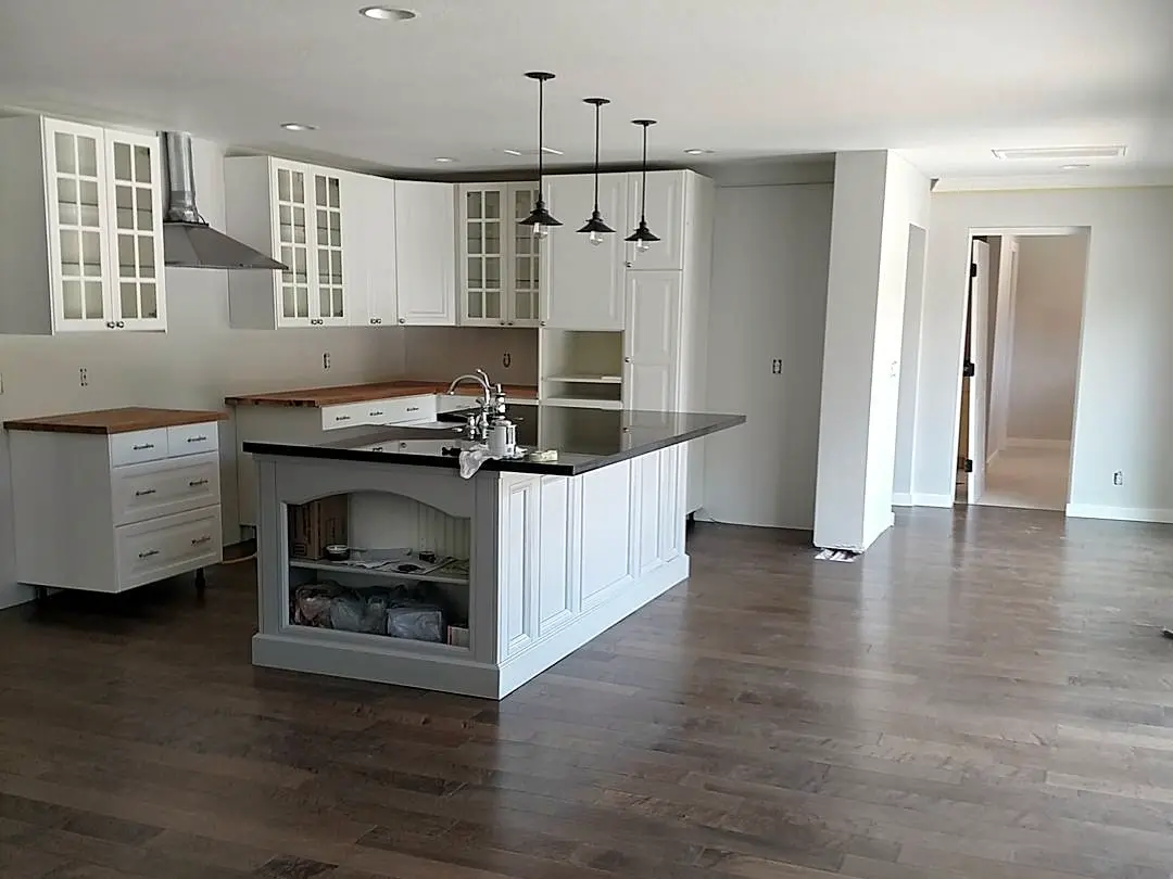 Open kitchen with white cabinetry, a dark island counter, pendant lights, and warm wood flooring.