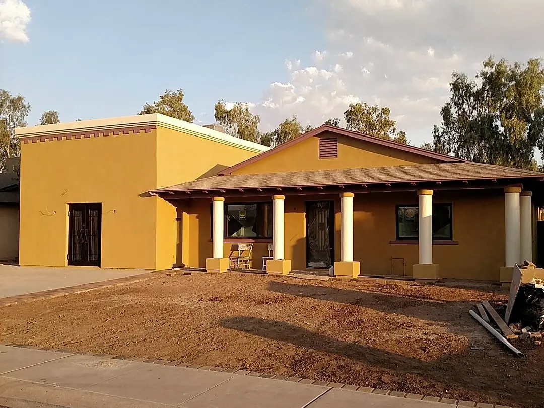 Finished mustard stucco residence with a shaded columned patio and dark red roof accents.