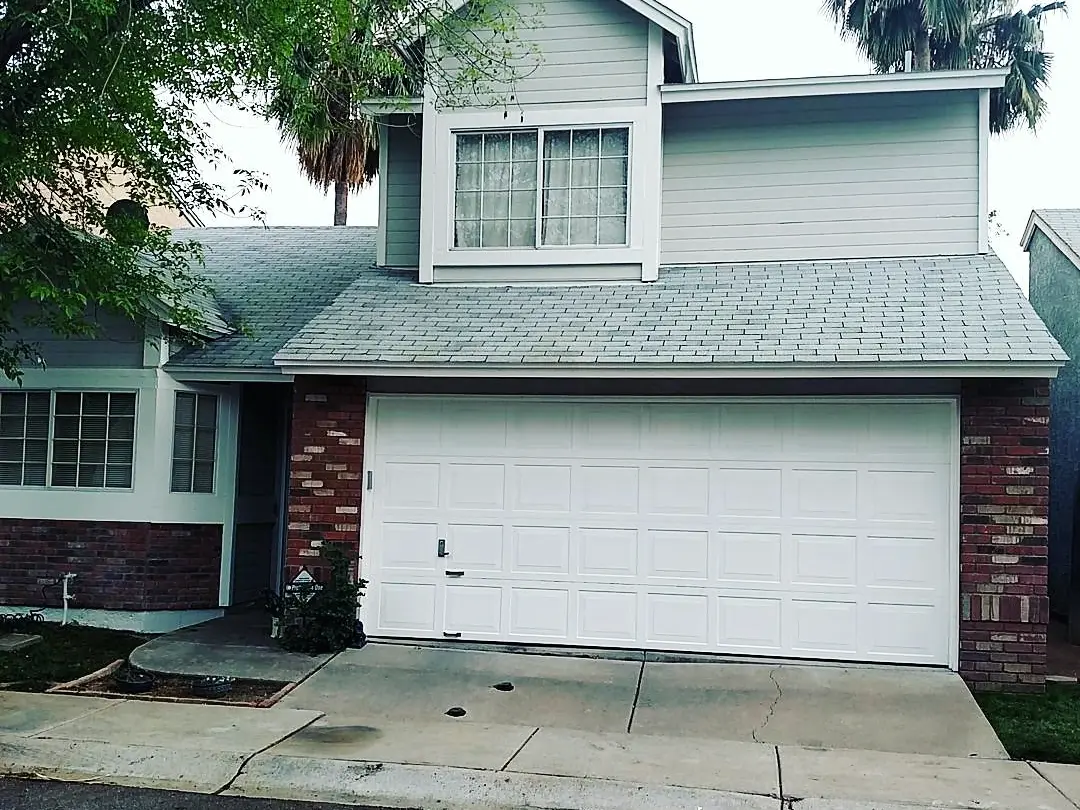 Two-story home finished in cool gray siding with white trim, a white garage door, and brick accents.