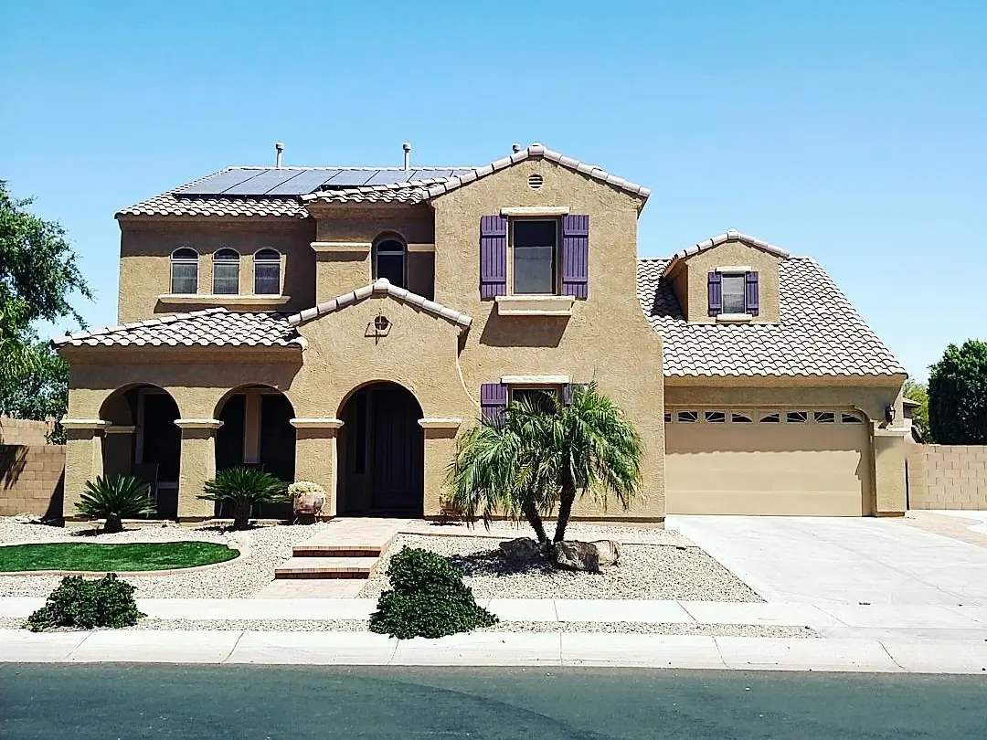 Two-story tan stucco home with purple shutters, a pale tiled roof, and desert landscaping.