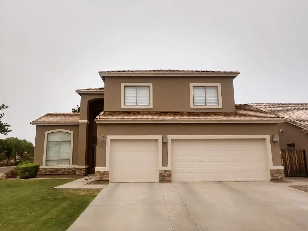 Two-story home finished in warm taupe and cream with stone accents and white garage doors.