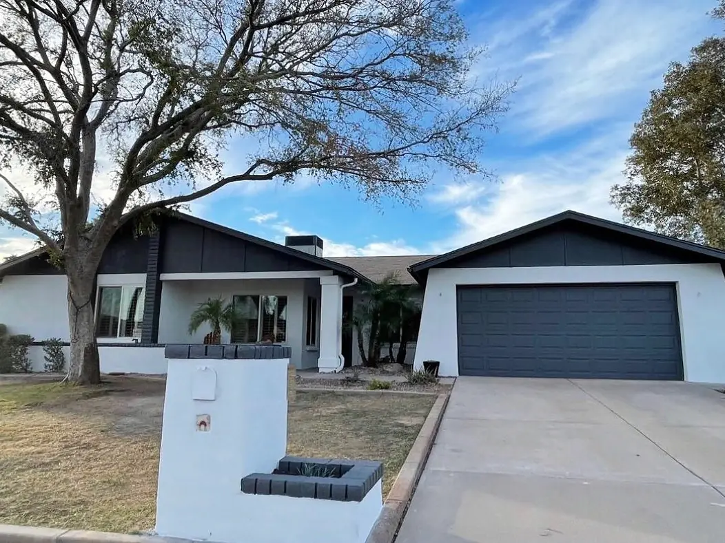 Modernized single-story home with crisp white stucco, charcoal gables and garage, and a blue sky overhead.