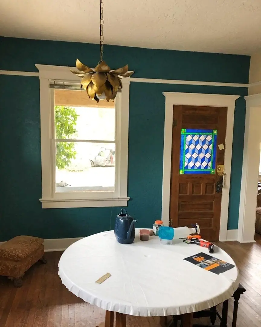Dining room with deep teal walls, bright white trim, wood floors, and a stained-glass front door.