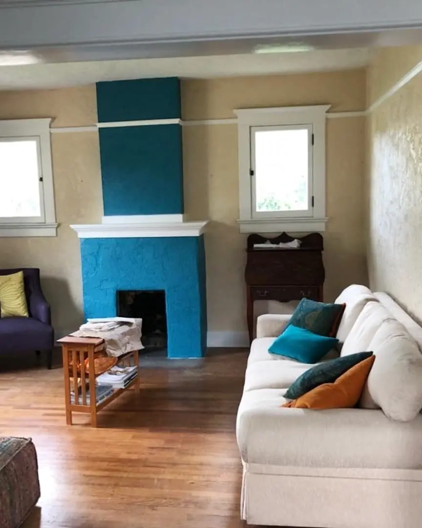 Lived-in room with a teal fireplace and accent wall, white trim, warm wood floors, and neutral furnishings.