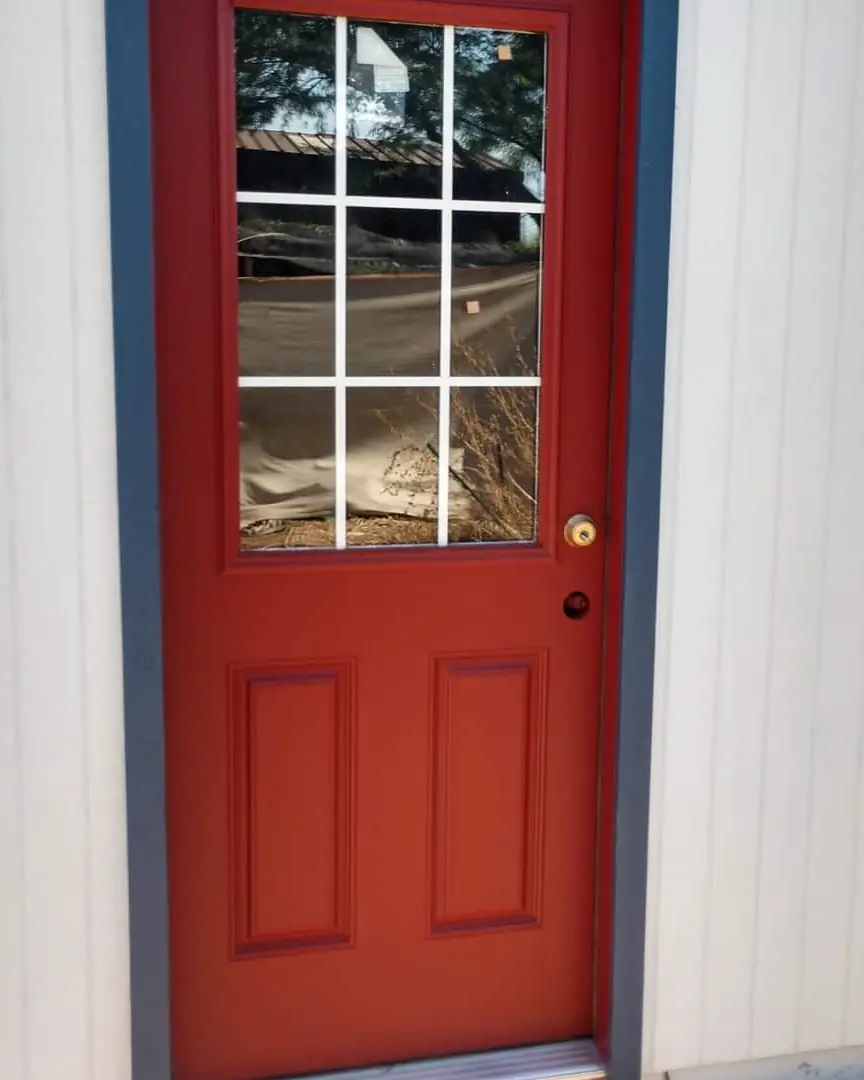 Close view of a deep red paneled door framed by dark blue-gray trim and pale vertical siding.