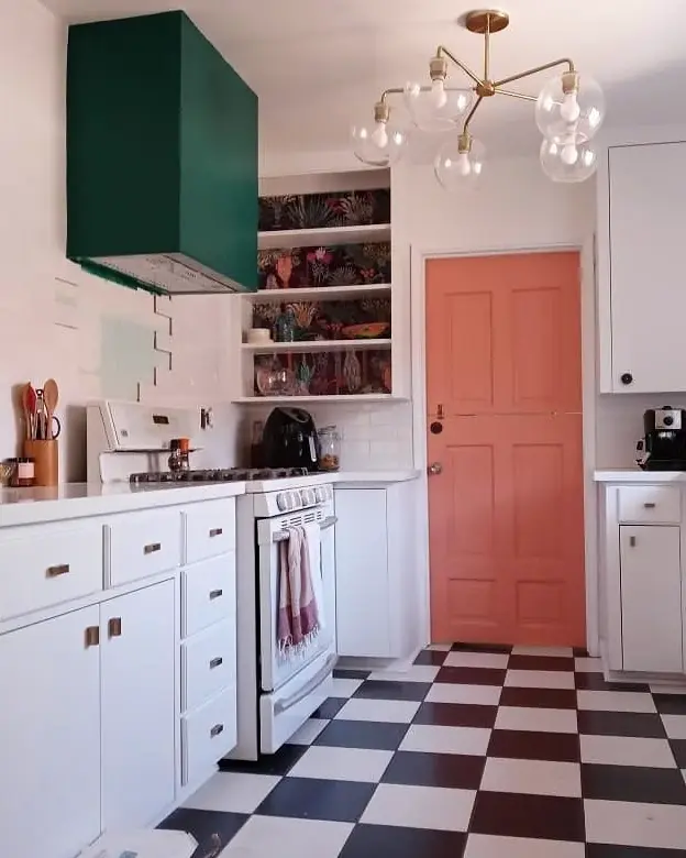 Bright kitchen with white cabinetry, a deep green range hood, coral door, and black-and-white checkerboard floor.
