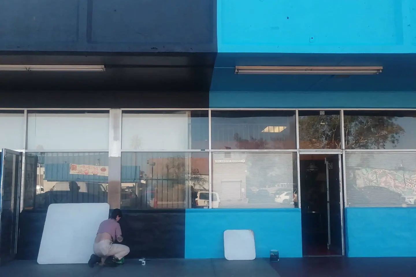 Painter working across navy and bright blue sections of a commercial storefront.