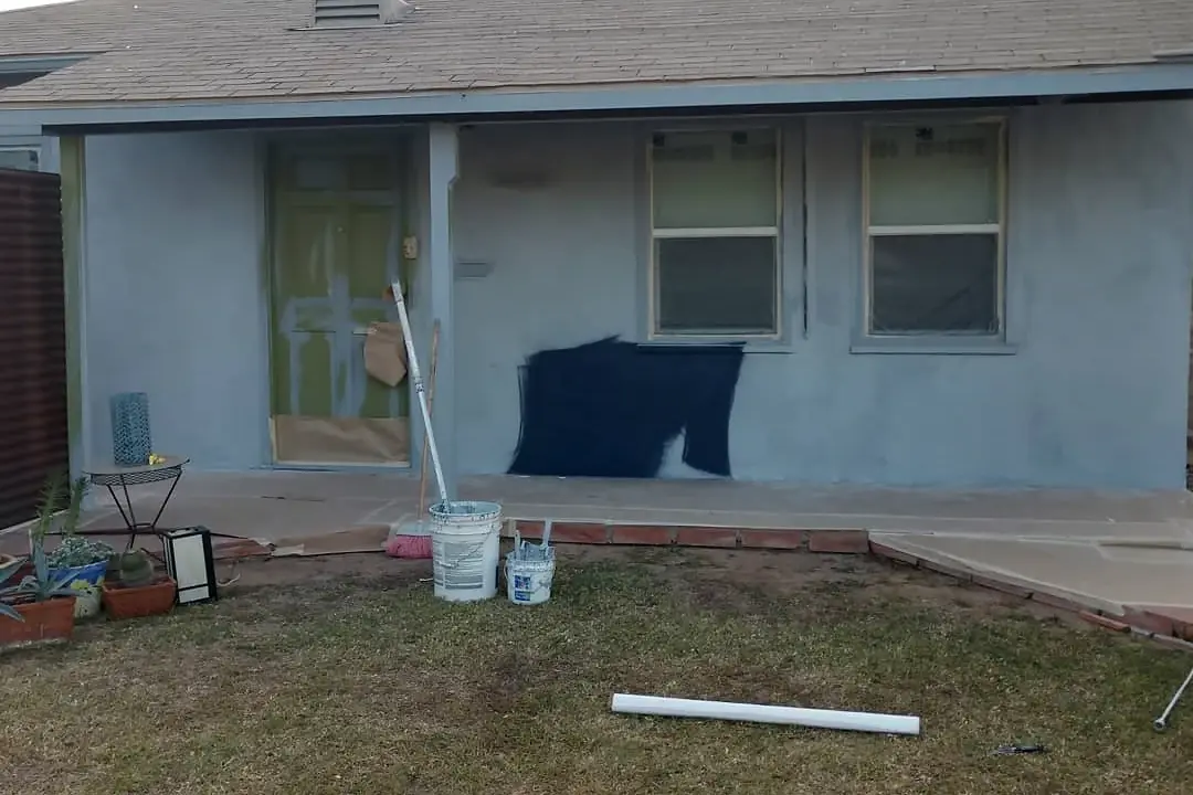Front wall in progress with windows masked, blue paint test areas, buckets, and preparation materials.
