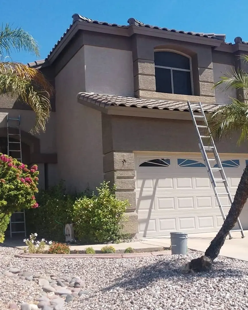 Two-story taupe stucco home during exterior work, with a tall ladder reaching the upper facade.