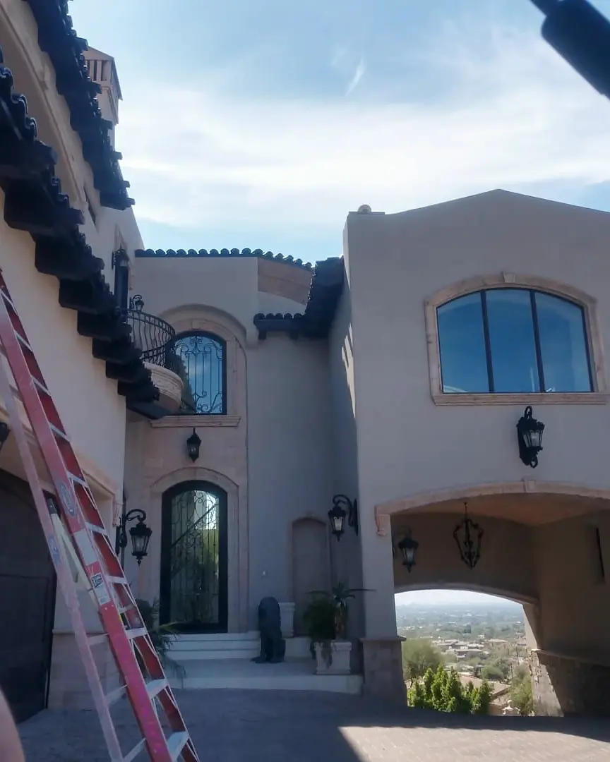 Tall ladder set against a two-story stucco home during upper exterior and roofline work.